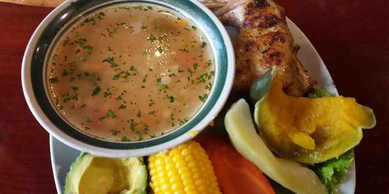 Plato que contiene un delicioso caldo de gallina guatemalteco con elote, zanahoria, wicoy, aguacate y tortillas, ideal para un almuerzo en familia