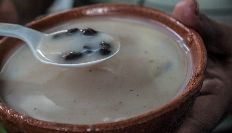 Delicioso atol blanco guatemalteco servido en una escudilla de barro,, se puede observar una cucharada de atol con frijoles negros.